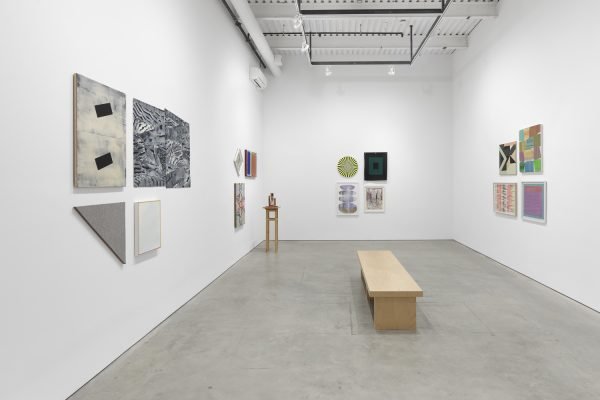 Installation view showing paintings on the wall, a sculpture in the left hand corner, and a bench in the middle of the gallery
